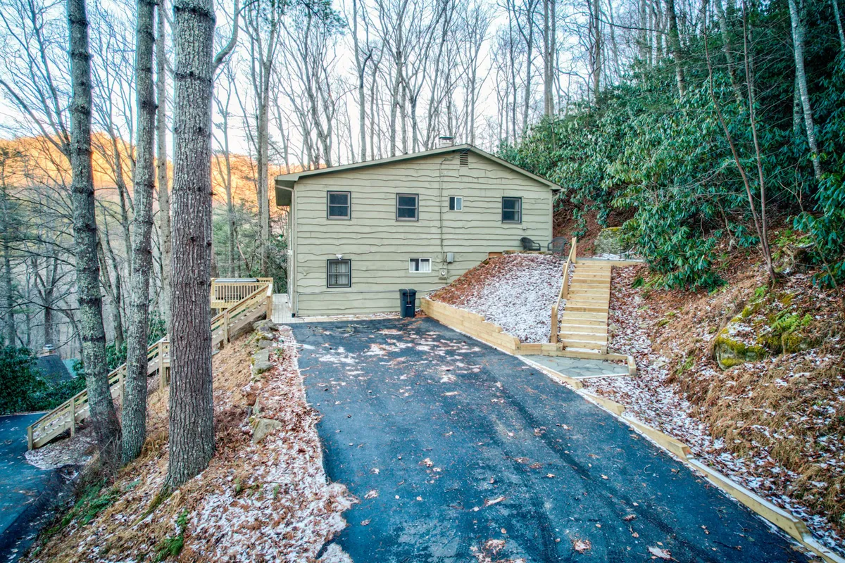 This image captures the exterior of the house, highlighting the driveway, surrounding trees, and the steps leading up to the house. The setting is calm and inviting, showing an accessible entrance and the peaceful natural environment that surrounds the property.