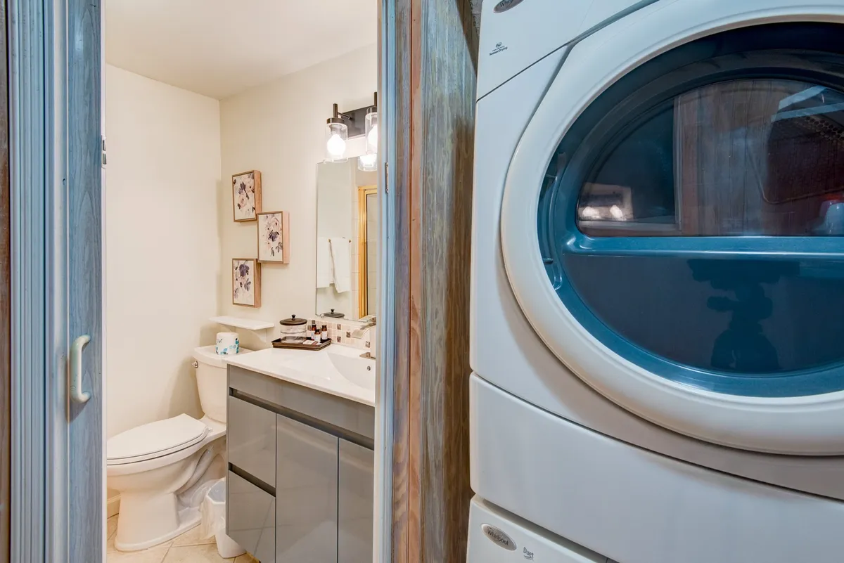 A practical laundry area features a washer, dryer, vanity with sink, and framed artwork, combining utility with cozy touches. The space serves both daily chores and personal grooming needs, vital for longer stays and larger groups.