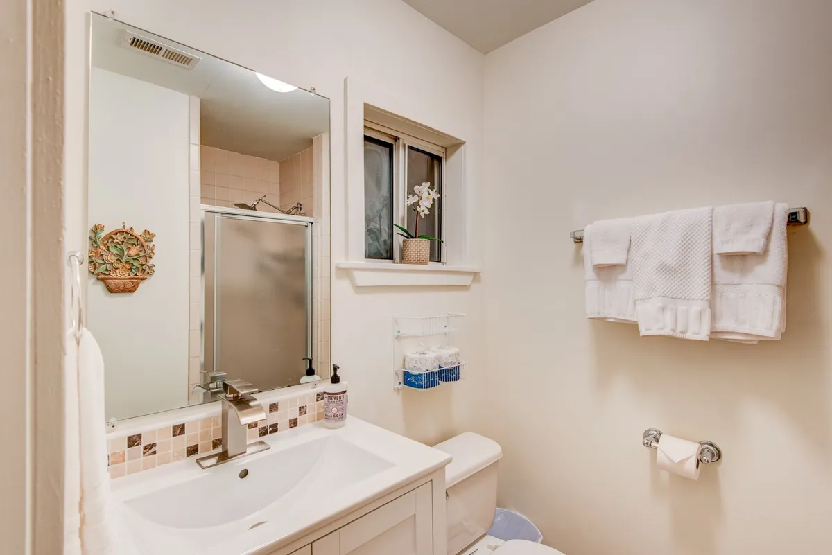 A modern full bathroom includes a sink, mirror, window, and shower, offering a calming and refreshing retreat for personal care. The design is functional yet serene, ensuring comfort for all guests.