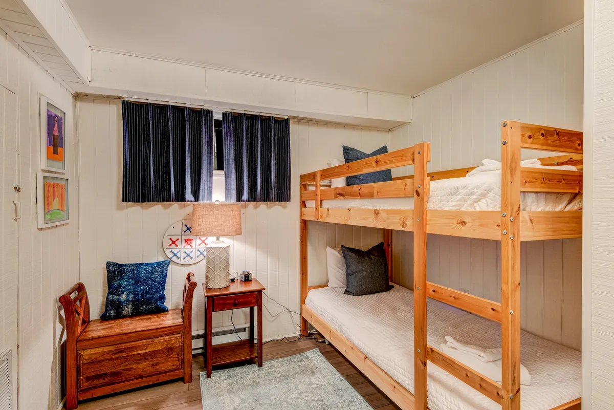 A welcoming nook with twin-over-twin bunk beds, a glowing lamp for bedtime reading, and playful artwork on the wall. The cozy space is ideal for children or extra guests, fostering late-night storytelling and playful adventures.