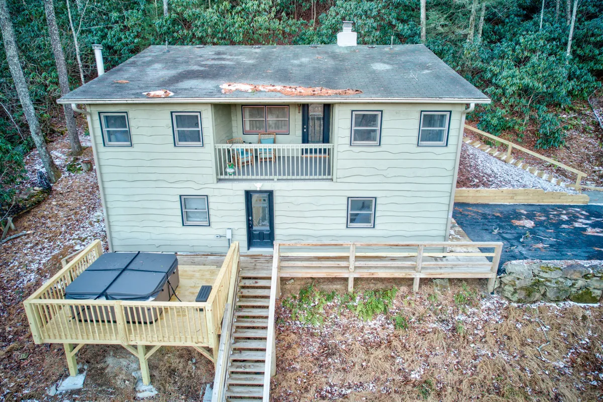 This exterior view captures the house, its balcony, and the surrounding greenery. The balcony is featured as a gathering spot, and the hot tub visible below adds another layer of outdoor enjoyment. The natural backdrop and peaceful mood invite relaxation, connection, and appreciation of the local landscape.
