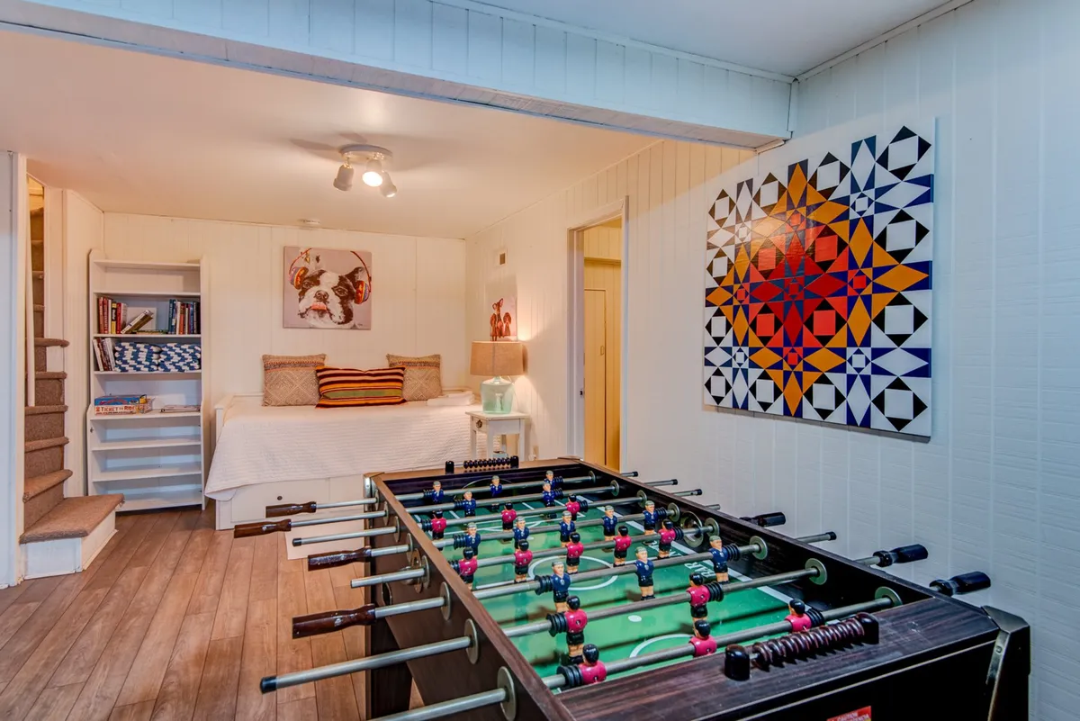 An interior shot featuring a foosball table, bed, colorful artwork, and bookshelf. The space is playful and relaxed, ideal for family game nights and unwinding together after a day outdoors.