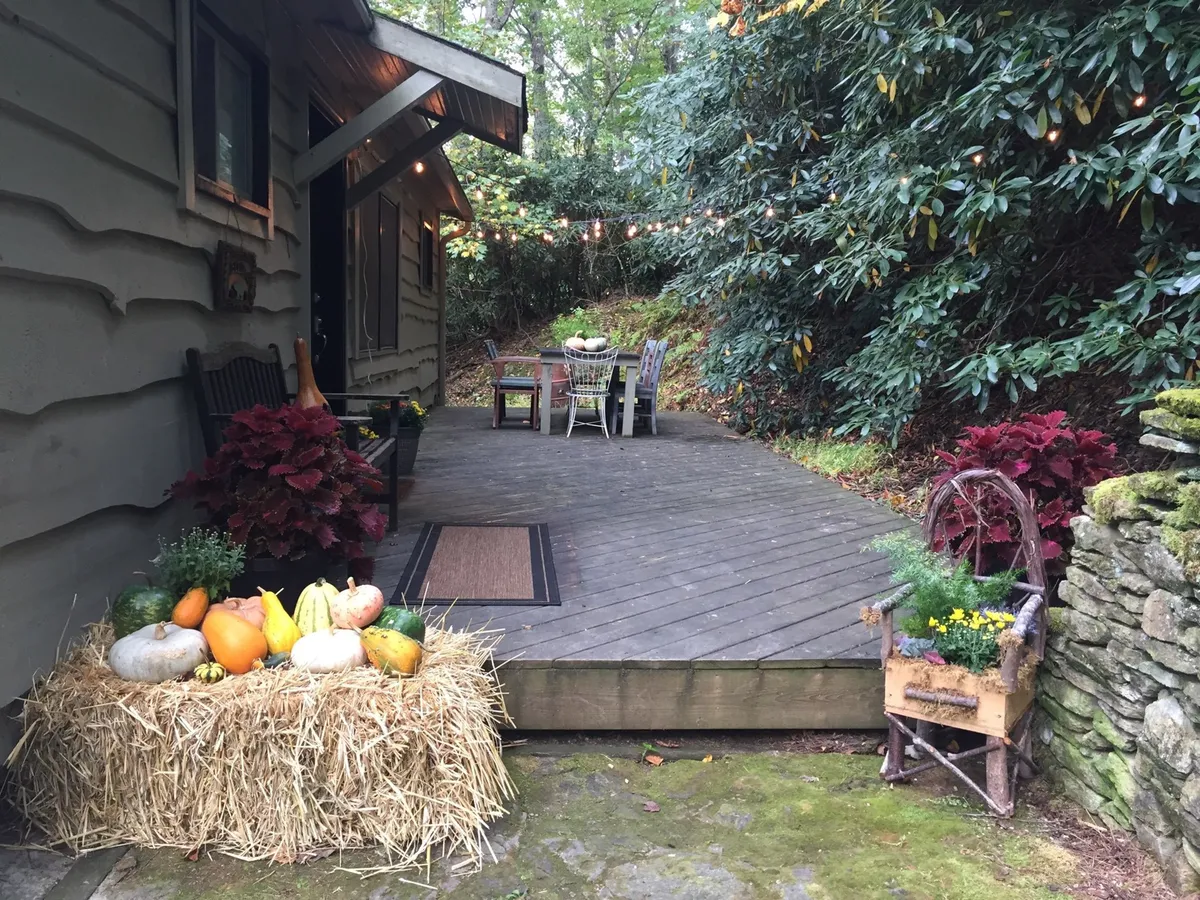 A welcoming outdoor dining area on a wooden deck, accented by lush greenery and a hay bale with fresh produce. The space is set up for casual gatherings or morning coffee, reinforcing the cabin’s connection to the outdoors and local bounty.