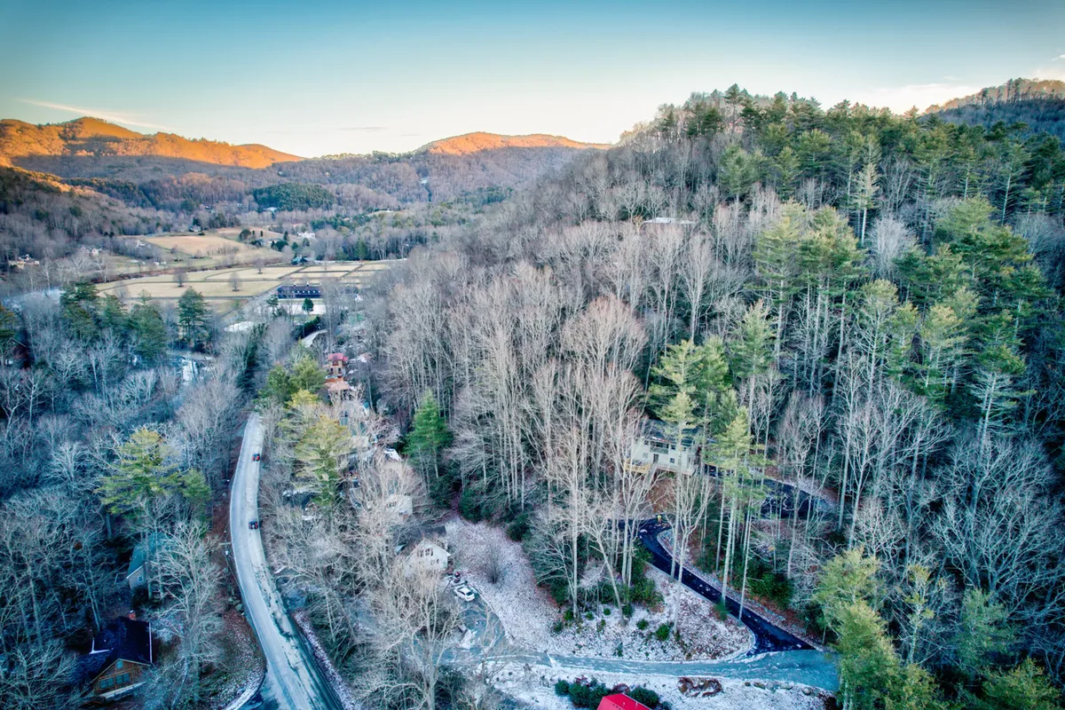 A sweeping view of rolling hills, dense forest, a winding road, scattered houses, and a mountain backdrop. This vista encapsulates the scenic beauty of the Valle Crucis area and invites exploration and adventure, making it easy to imagine setting out from the cabin to visit landmarks like the Mast General Store Annex.