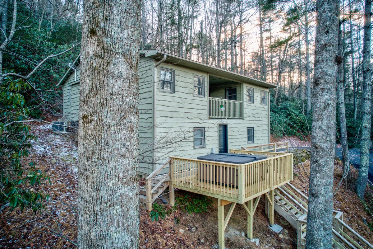 This image features the exterior wooden deck of the cabin, complete with a hot tub, the house facade, and surrounding trees. The peaceful setting highlights the connection between the cabin and its natural surroundings, hinting at opportunities for relaxing outdoors and listening to the sounds of the area, such as live music drifting from nearby venues.