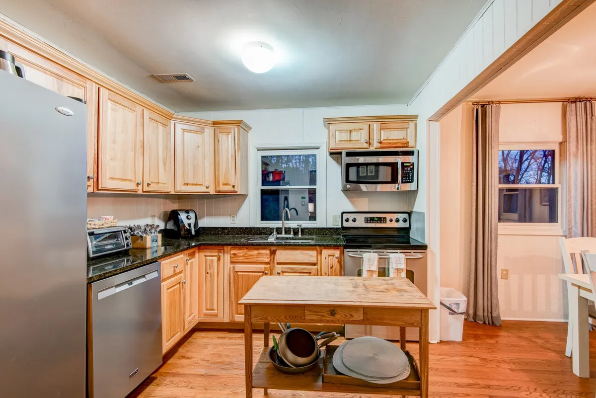 The kitchen is showcased with wooden cabinets, a central island, and modern stainless steel appliances, including a large window that brings the outdoors in. The space is inviting for meal preparation and group interaction.