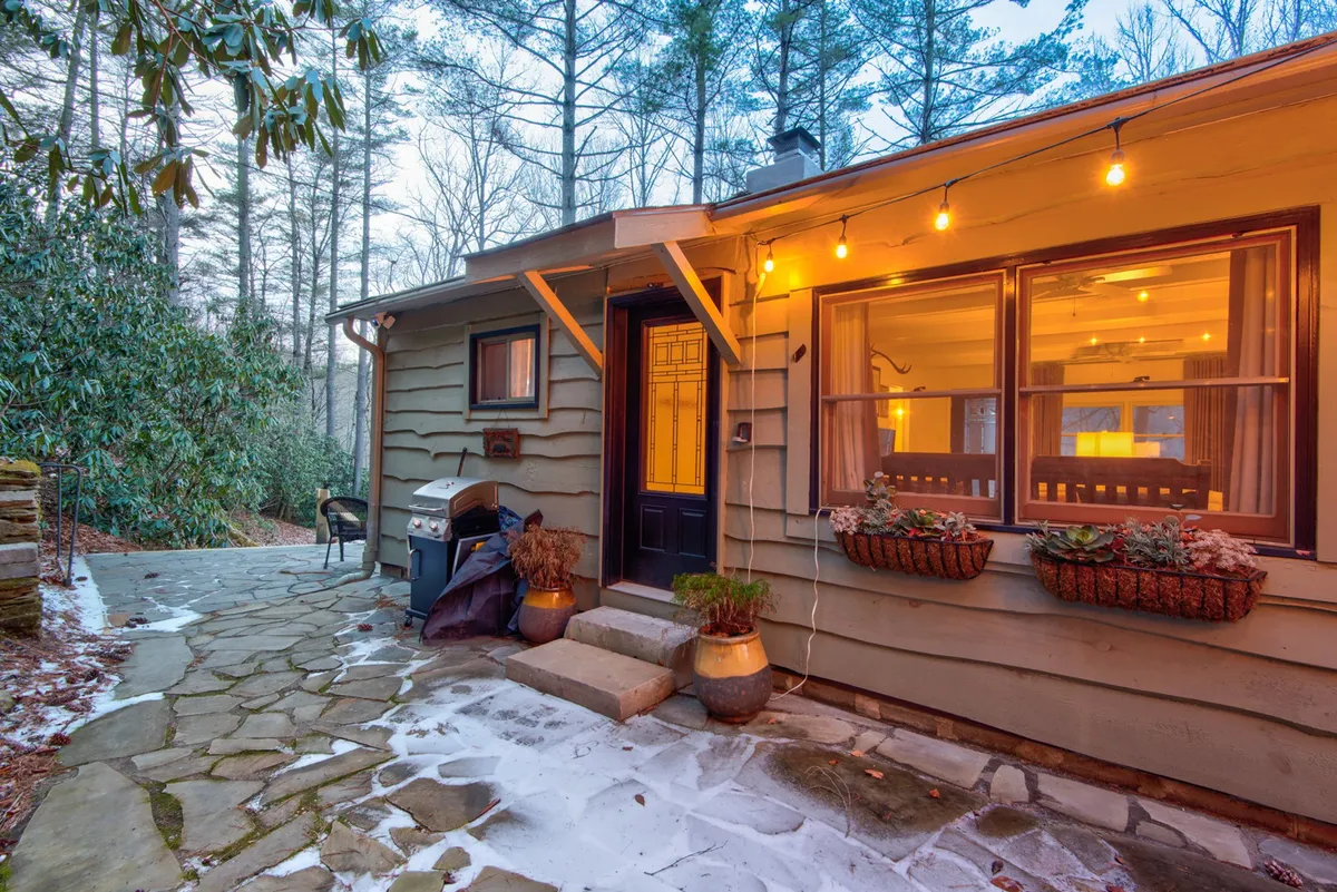 The hero image showcases the cozy exterior of Orchid Cabin, featuring an inviting front door, a charming outdoor seating area perfect for gatherings, and decorative planters that add a welcoming touch. The setting hints at evenings spent relaxing outdoors, with space for barbecuing and dining against the peaceful North Carolina mountain backdrop.