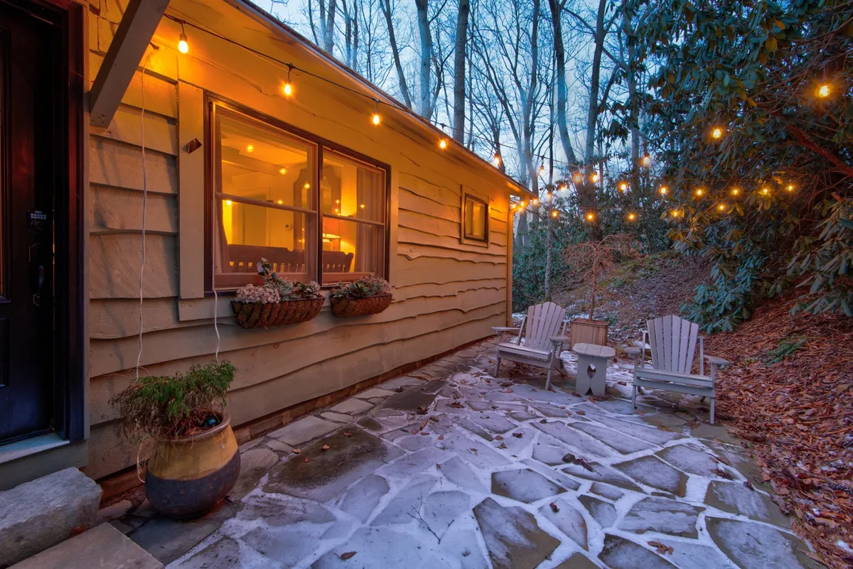 An intimate outdoor area lit by warm string lights, featuring wooden chairs and a stone pathway. The glow of a nearby window gives a sense of coziness and invites evening relaxation. The setting is perfect for stargazing, reading, or sharing quiet moments, offering a more secluded nook for guests.