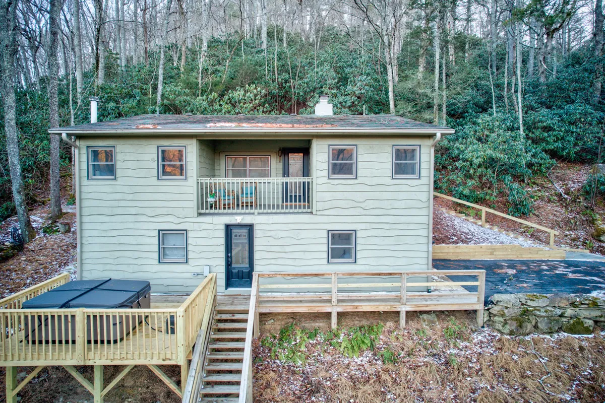 This image features a two-story house with a spacious balcony overlooking the surrounding trees and a welcoming deck area. The balcony is furnished for relaxation and offers a view ideal for enjoying coffee or gathering with family. The peaceful, natural setting connects the home to its environment, suggesting both privacy and accessibility.